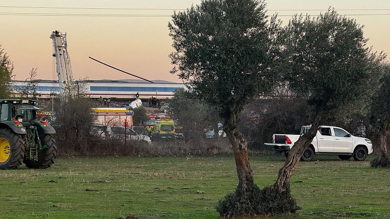 Atardecer en zona rural con un tren detenido, personal de emergencias, una grúa industrial, un camión de bomberos, un tractor y una camioneta blanca.