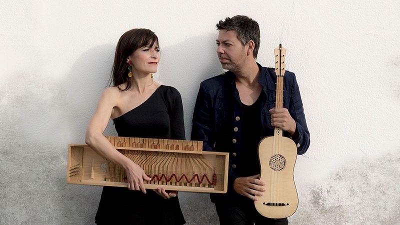 Los m�sicos Sara Marina y Emilio Villalba, del conjunto Sephardica, posan juntos frente a una pared blanca sosteniendo instrumentos hist�ricos de madera.