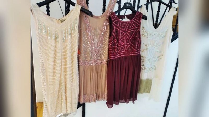 Cuatro vestidos de fiesta femeninos de inspiración vintage y estilo años 20 con lentejuelas y abalorios, colgados en una barandilla.