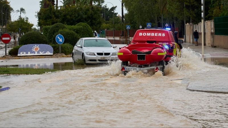 Vehículo de bomberos circulando por una calle inundada con una embarcación de rescate en Oliva durante un episodio de lluvias torrenciales.