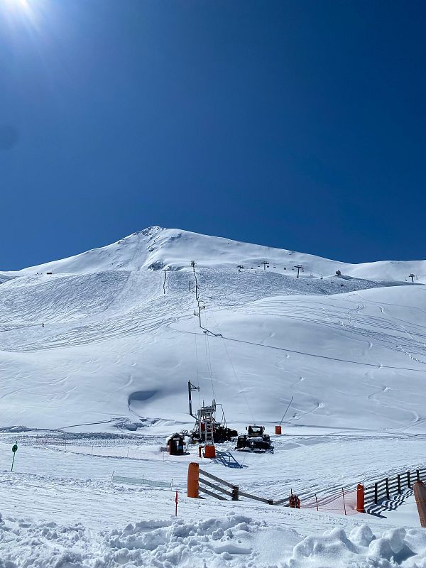Impresionante paisaje nevado en una estación de esquí, con pistas, remontes y máquinas pisanieves.  Cielo azul intenso y sol brillante.