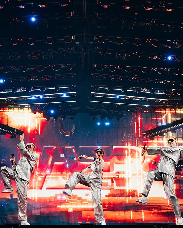 Artistas islandeses con trajes plateados ensayan una coreografía dinámica en un escenario iluminado con luces rojas y anaranjadas para Eurovisión 2025.