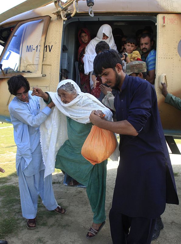Men assist woman and others evacuating flood waters in Kalam, after they arrived by helicopter to a military base in Khuazakhela in Swat district
