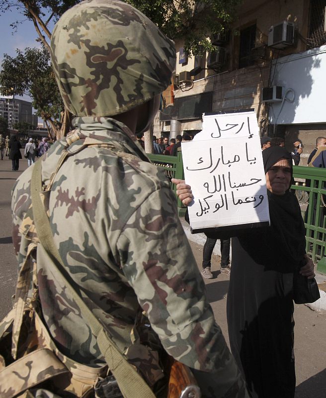 Una mujer se pasea delante de un soldado con un cartel en el que se puede leer "Mubarak, vete. Dios nos ayuda".