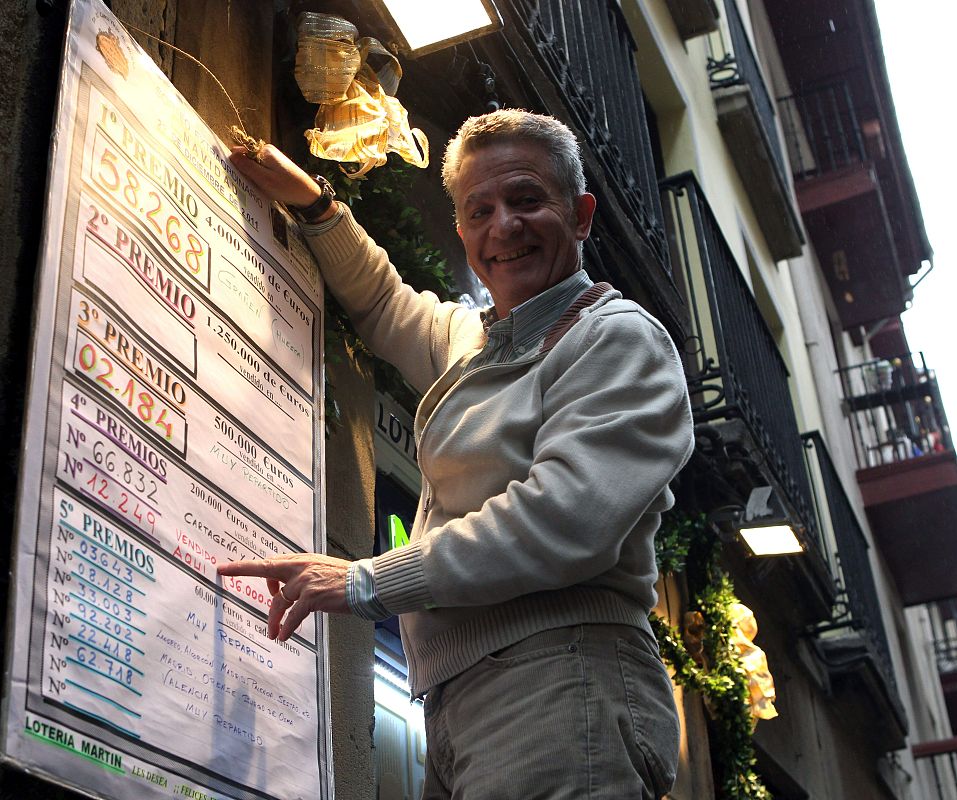 Un lotero con el cartel de uno de los cuartos premios, dotados con 200.000 euros a la serie, repartido en la administración número dos de Bilbao, con el número 12.249, del que han vendido 36 millones de euros.