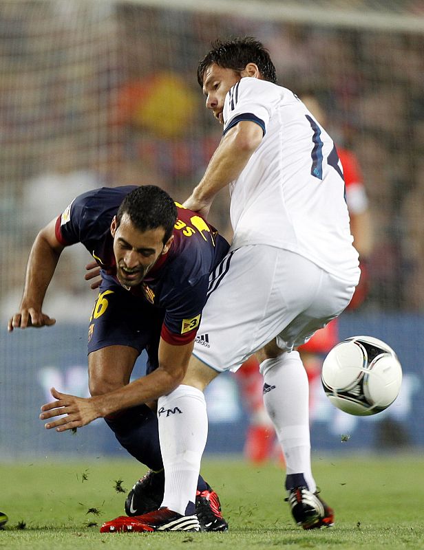 Xabi Alonso y Sergio Busquets disputando un balón en el centro del campo.
