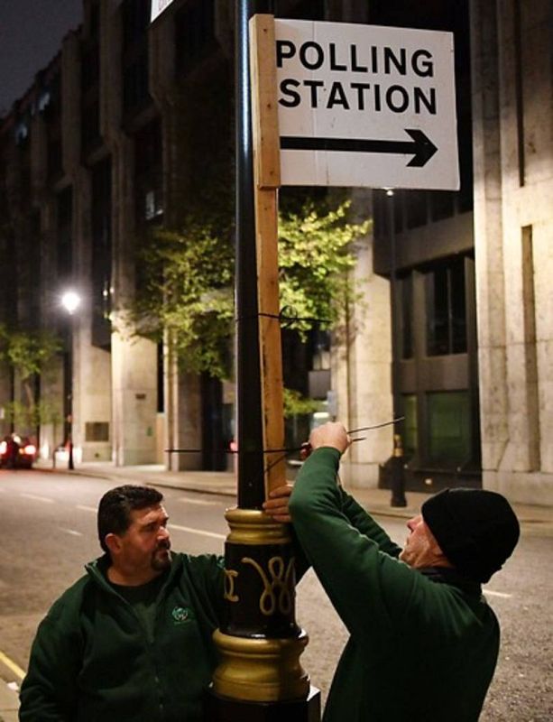 Unos trabajadores pegan un cartel en una farola en Londres mientras se abren los colegios electorales.