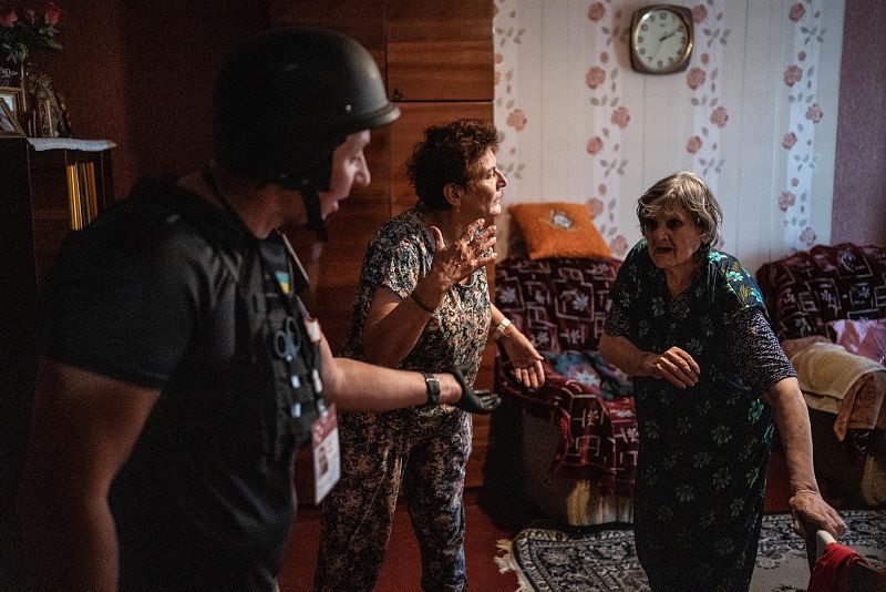 Evacuación de una mujer mayor de su apartamento durante la guerra.  Se observa angustia en la mujer y la asistencia de otra persona, posiblemente un militar.