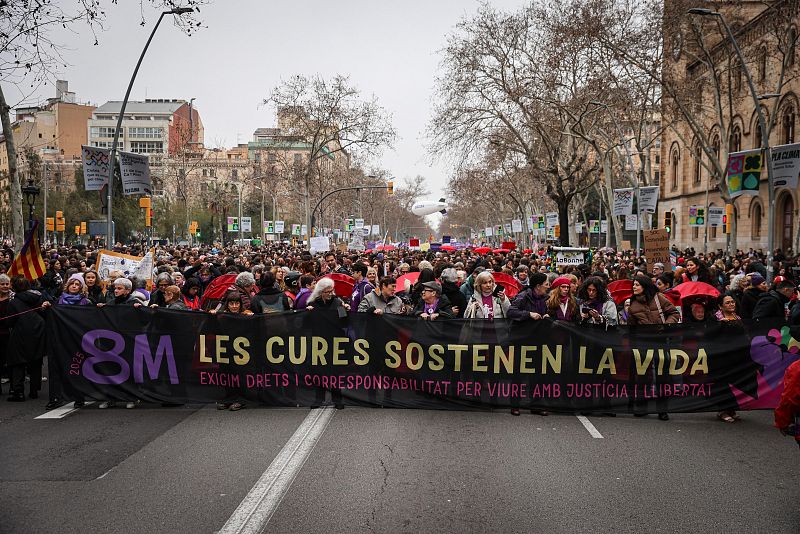 Multitud en manifestación del 8M 2023 en Barcelona. Gran pancarta negra con letras rosas y doradas: "Los cuidados sostienen la vida. Exigimos derechos y corresponsabilidad para vivir con justicia y libertad".  Marcha por avenida arbolada.
