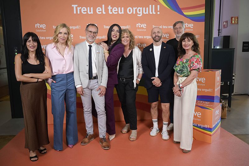 Grupo de ocho personas con ropa informal, posando ante un fondo naranja con arcoíris y el lema "Treu el teu orgull!" junto al logo de RTVE Catalunya. Orgullo 2025.