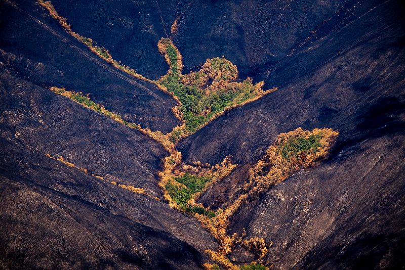 Vista aérea de una montaña tras un incendio. Predomina el color oscuro en la ladera, contrastando con zonas verdes que sobrevivieron al fuego.