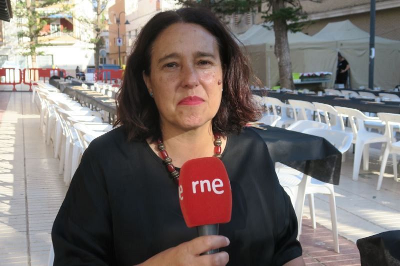 Mariló Gradolí, presidenta de una asociación de víctimas, sostiene un micrófono de RNE. Se encuentra en un evento al aire libre, con sillas y carpas blancas como telón de fondo.