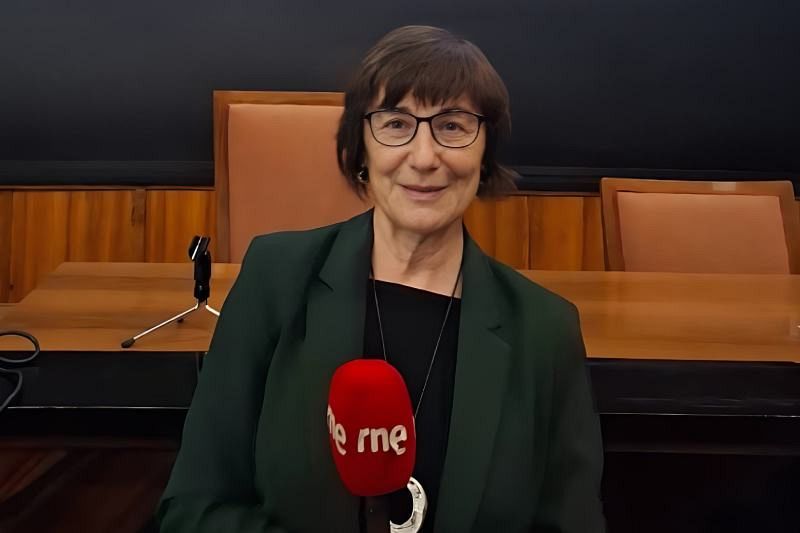 Carmen Magallón, con gafas y cabello castaño, está sentada frente a un micrófono rojo con el logo de una emisora de radio. Lleva una chaqueta verde oscura y un collar plateado, en una sala con sillas naranjas.