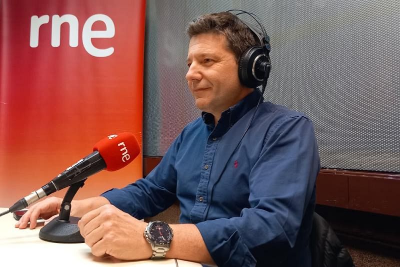 Alfredo García, operador de la central nuclear de Ascó, está en un estudio de radio frente a un micrófono con el logo de RNE. Viste una camisa azul y auriculares, con un panel de RNE al fondo.