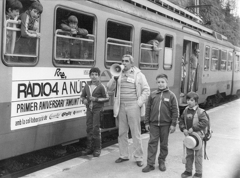 Tren en estación de montaña con pancarta de Ràdio 4 y Salvador Escamilla con megáfono. Celebración del primer aniversario en Núria.