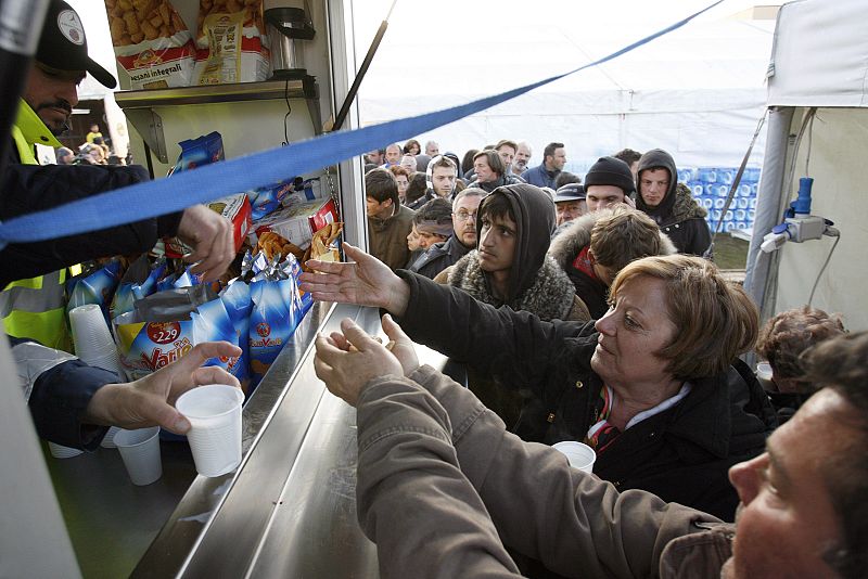 Los damnificados hacen cola para conseguir comida en el campo de víctimas de Paganica.