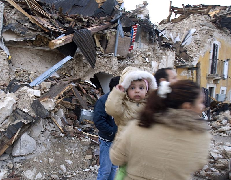Una mujer con su bebé inspeccionan el estado de los edificios en Onna, Italia.