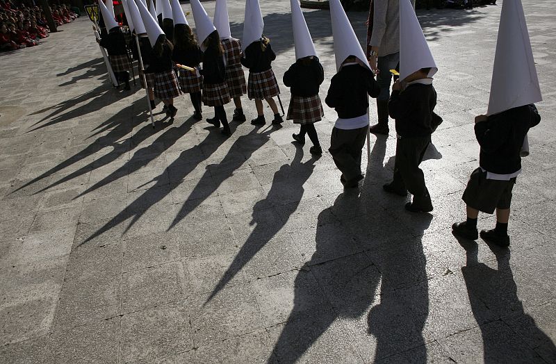Children wearing hoods dressed as penitents take part in a procession in a school three days before the start of Holy Week in Seville