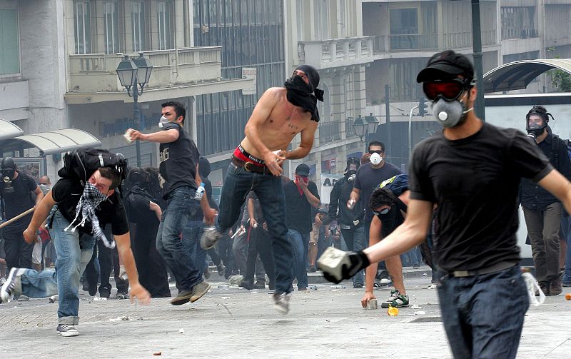 Unos manifestantes lanzan adoquines a unos agentes de la policía antidisturbios durante .un acto de protesta frente al Parlamento griego
