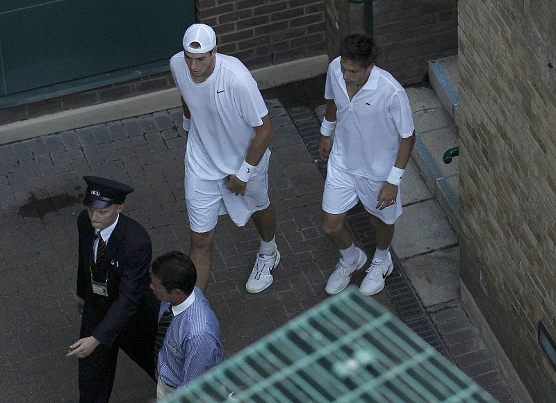 Los jugadores Nicolas Mahut y John Isner son escoltados a la zona de vestuarios.