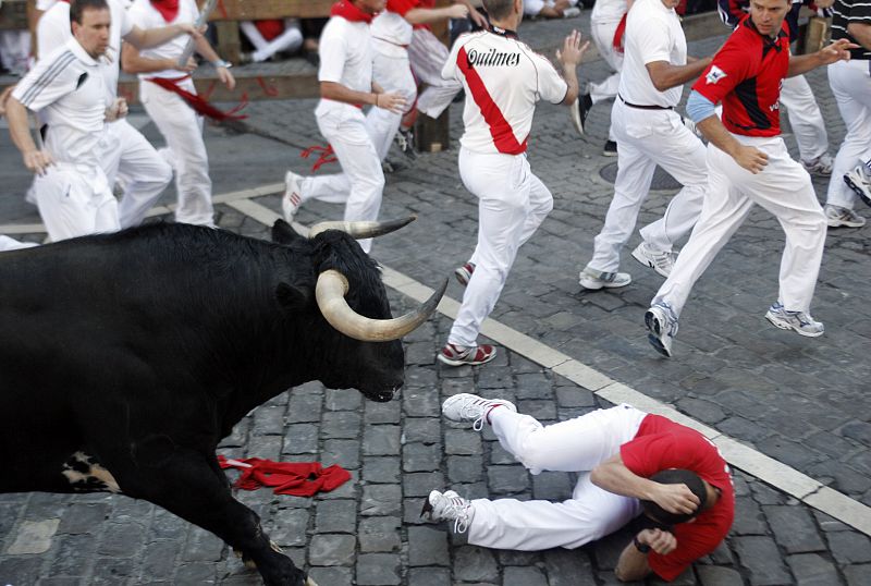 A runner falls in front of a Penajara fighting bull on the first day of the running of the bulls during the San Fermin festival in Pamplona