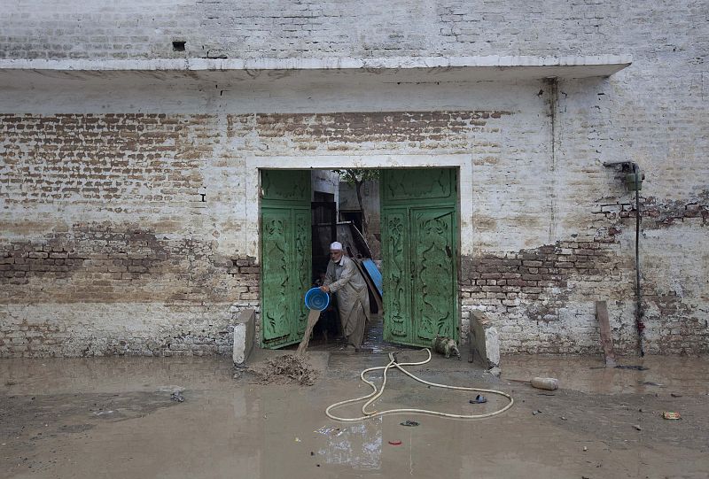 A man uses a bucket to clear flood waters after returning to his house in Nowshera