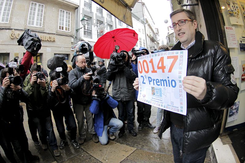 El administrador del despacho de lotería Nª3 de la Rúa del Vilar (Santiago de Compostela), José Luis Tojo Núñez, muestra el cartel con el número 00147, agraciado con con el segundo premio de la Lotería de Navidad.