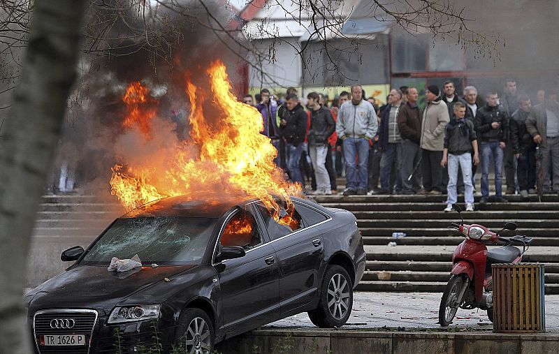Un coche arde durante los disturbios ante la mirada de los manifestantes albaneses.