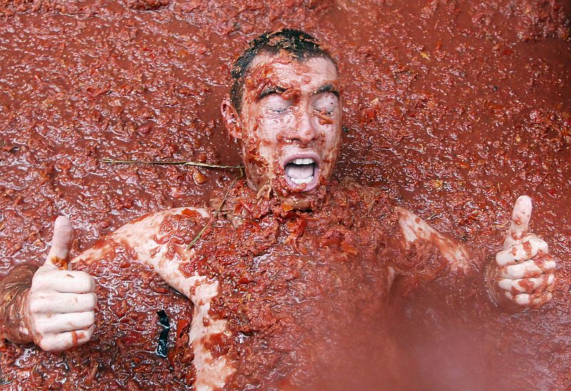 Un jóven hace un gesto de aprobación mientras se sumerge en un río de tomates