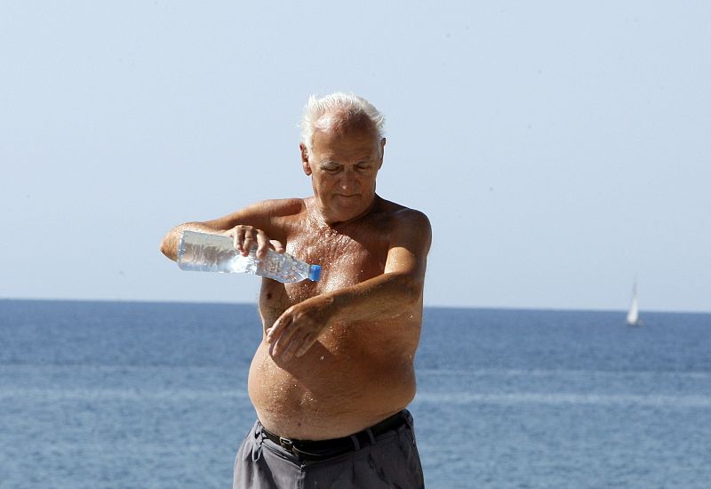 Un hombre se refresa el cuerpo en la playa de la Barceloneta con una botella de agua