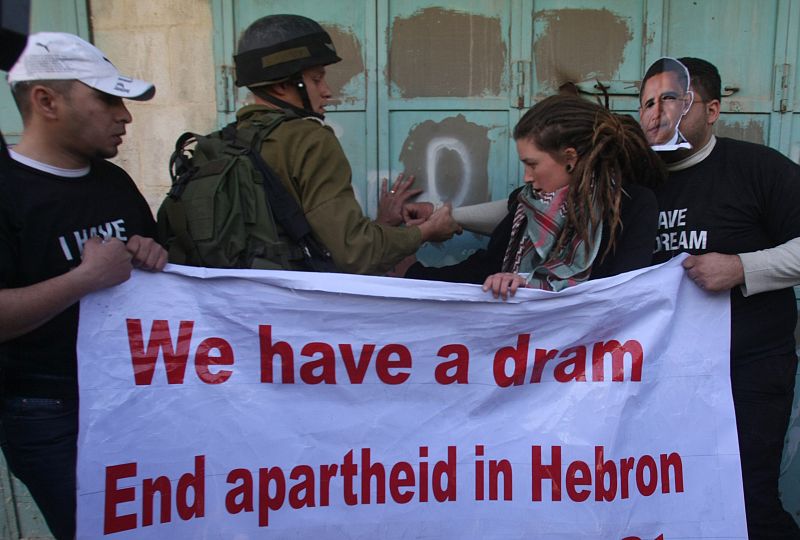 Un soldado israelí dispersa una manifestación de activistas palestinos que sostienen un cartel en el que parafrasean a Martin Luther King con el lema "Tengo un sueño, que finalice el apartheid en Hebrón"