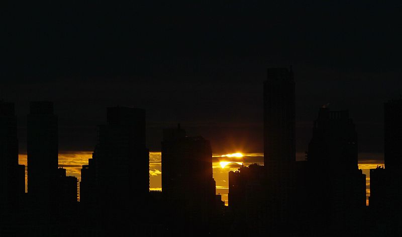 The sun rises behind the skyline of Manhattan as it is partially eclipsed by the moon during a hybrid eclipse over New York