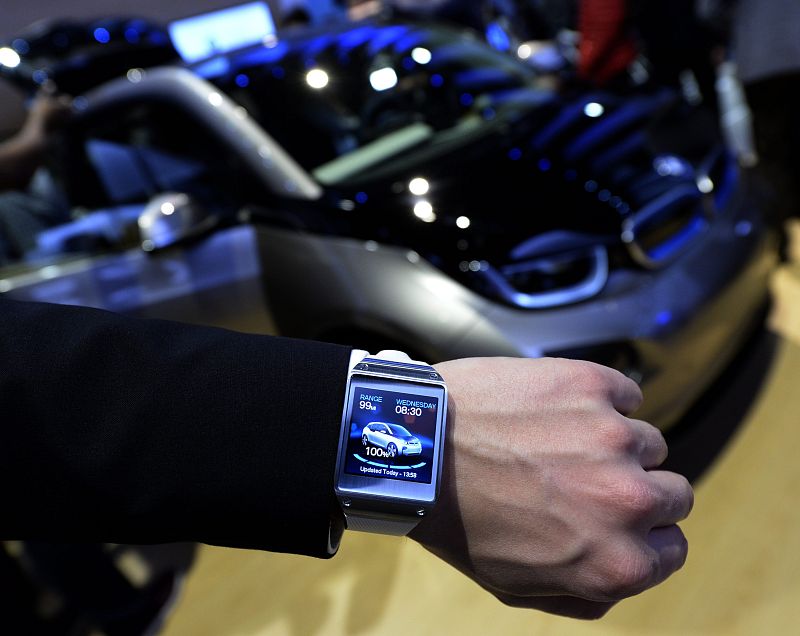 Un expositor muestra un reloj inteligente Samsung mientras este interactúa con un vehículo eléctrico BMW 3i