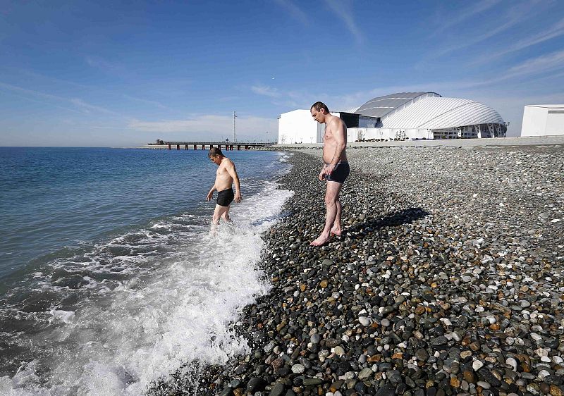 Men wade into the sea on a sunny day as the Olympic Park is seen in the background, during the 2014 Winter Olympic Games in Sochi