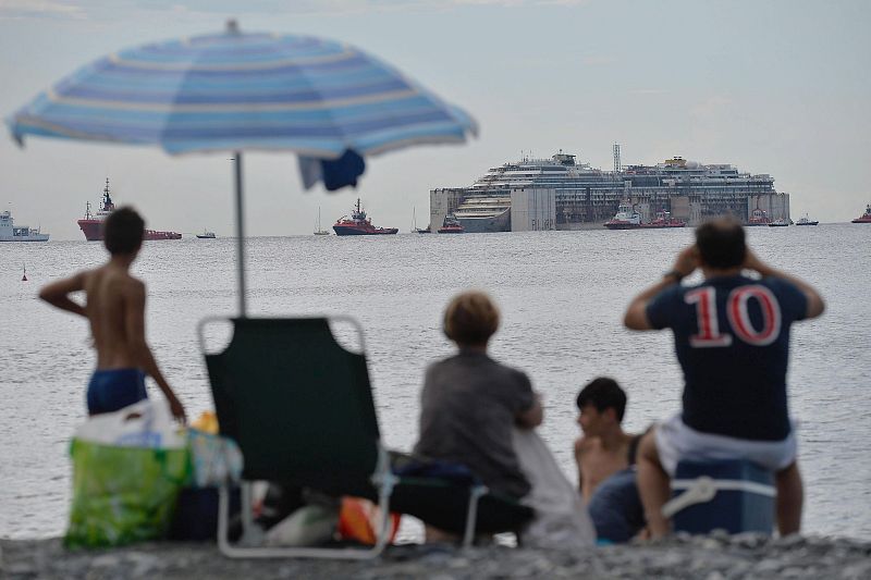 Varias personas miran desde la playa de Génova (Italia) la llegada del Costa Concordia.
