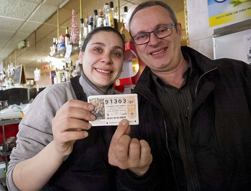 Miriam Gómez, dueña del bar Los Amigos (Badajoz) y un cliente, Manuel González, muestran un décimo del número 91.363