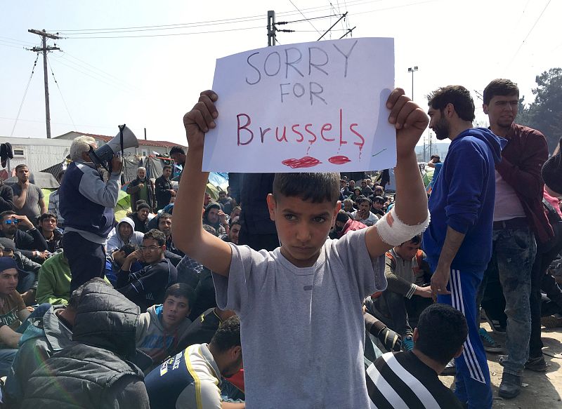 Un refugiado en la frontera macedonia sostiene un cartel que reza "Lo sentimos, Bruselas", en señal de condolencia