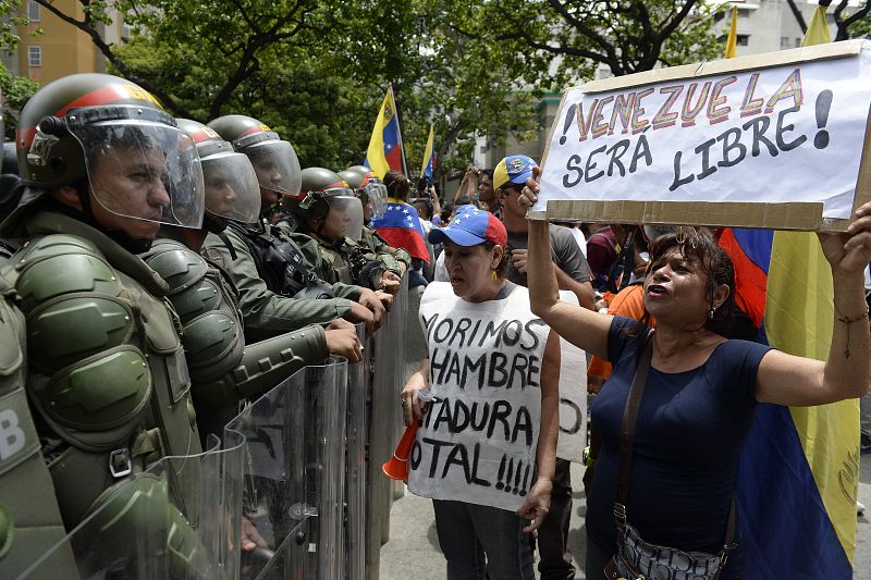 Dos mujeres portando sendas pancartas que rezan "Venezuela será libre" y "Morimos de hambre. Dictadura total".
