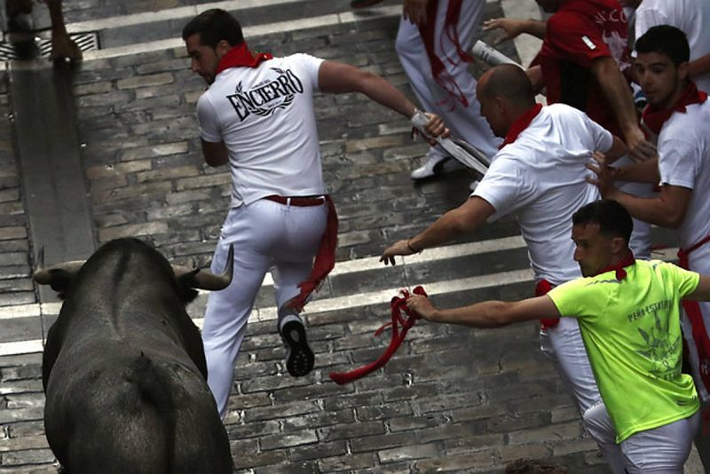 Varios mozos ante un toro de la ganadería de José Escolar tras pasar Mercaderes, en el tercer encierro