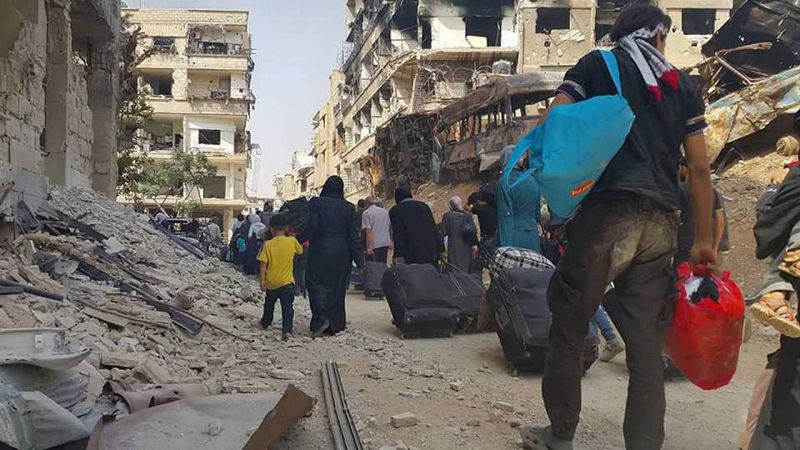 Varios habitantes de Daraya se dirigen a la explanada donde aguardan los autobuses para la evacuación