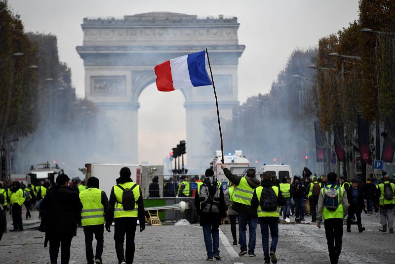 Un grupo de "chalecos amarillos" avanza por los Campos Elíseos ondeando una bandera de Francia