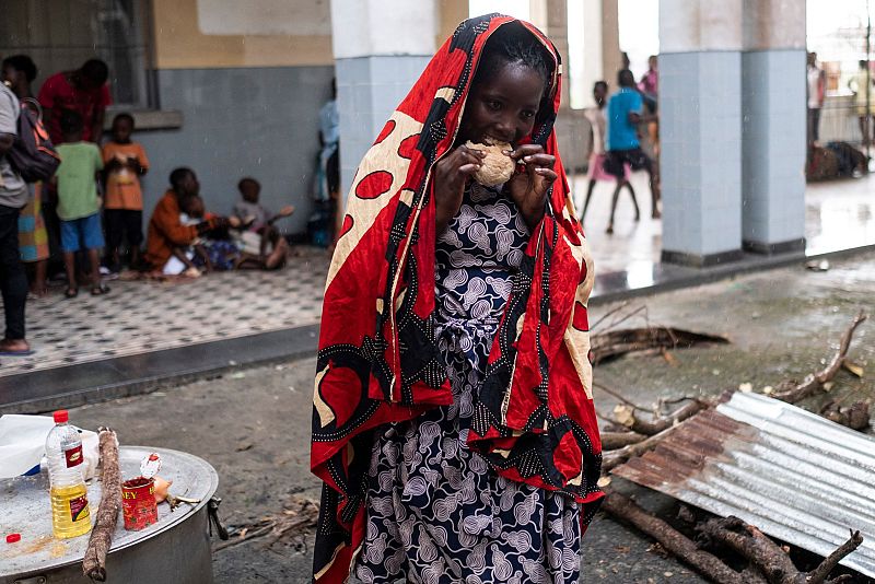 Una mujer se protege de la lluvia con un pañuelo mientras come un pedazo de pan en un campamento de refugiados improvisado en un instituto de Beira, Mozambique