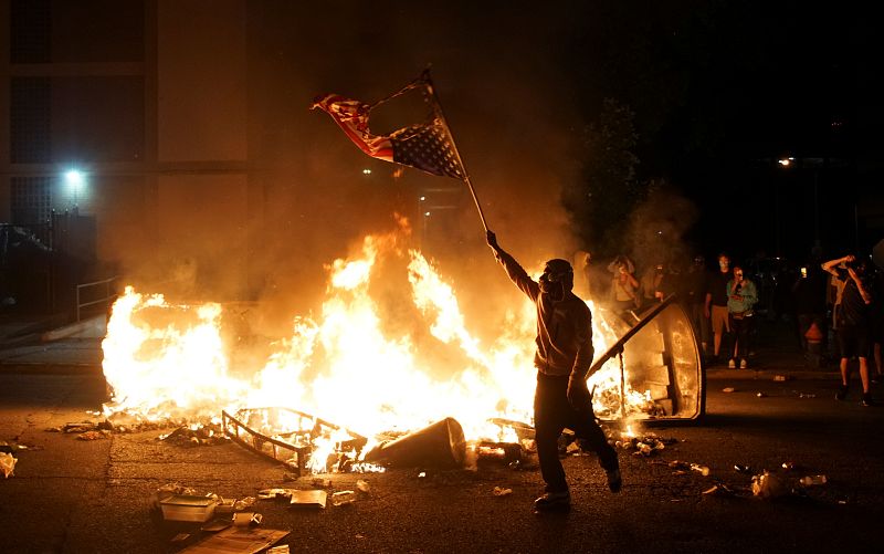 Un manifestante agita la bandera estadounidense quemada en una hoguera en Missouri