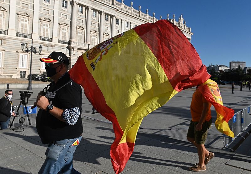 Un grupo de personas con banderas de España como homenaje a las victimas en las inmediaciones del Patio de la Armería del Palacio Real en Madrid.