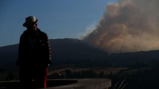 Un hombre camina con la columna de humo de fondo desde el Mirador da Capela en Pobra de Brollón