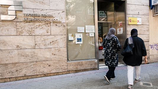 Varias personas migrantes esperan en el exterior de una oficina de la Seguridad Social