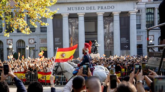 Varias personas disfrutan del desfile durante el acto solemne de homenaje a la bandera nacional y desfile militar por el 12 de octubre, D�a de la Hispanidad, en la Plaza de C�novas del Castillo, a 12 de octubre de 2026, en Madrid (Espa�a).
