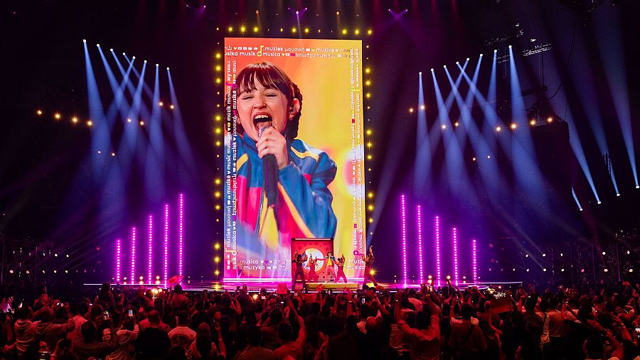 Chloe DelaRosa en el escenario de Eurovisión Junior 2024 con bailarines y una gran pantalla al fondo.