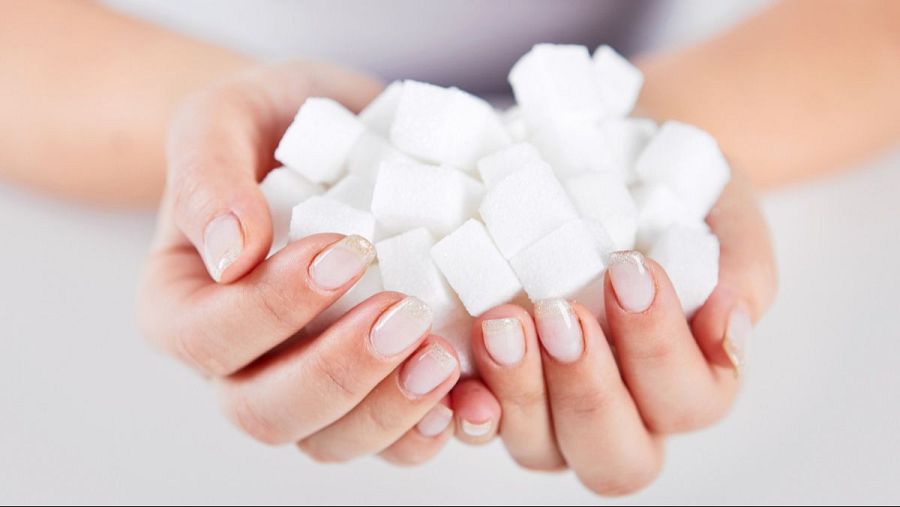 Manos con manicura francesa sujetan terrones de azúcar, representando el consumo de este producto.