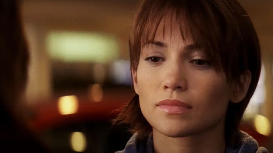 Jennifer López en una escena de "Nunca más", con el pelo corto y una expresión seria. Lleva una sudadera oscura y el fondo está desenfocado.